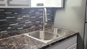 Cucina con lavello a due vasche, rubinetto in acciaio inossidabile e schienale con motivo geometrico.
