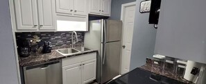 A compact kitchen with white cabinets, a stainless steel refrigerator, a double sink, and a black countertop. - Private getaway by the beach (Pensacola)