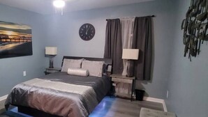 Una camera da letto con un letto, una sveglia, un quadro e un televisore appeso al muro.