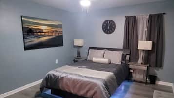 A bedroom with a bed, a clock, a painting, and a TV on the wall.