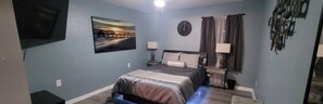 A bedroom with a bed, a clock, a painting, and a TV on the wall. - Private getaway by the beach (Pensacola)