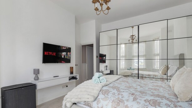 Une chambre à coucher moderne avec un grand lit, un téléviseur fixé au mur, un miroir et une commode.