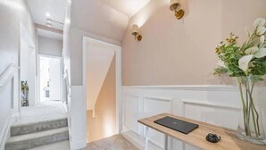 Un couloir avec un escalier menant à une autre pièce, un petit bureau avec un ordinateur portable et un vase rempli de fleurs.