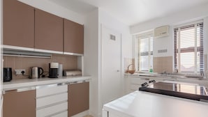 A modern kitchen with white and brown cabinets, a stainless steel range, and a window with blinds. - Elegant 1BR Flat in Westminster Near Victoria Tube (London)