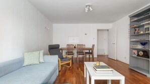 A living room with a sofa, chairs, a dining table, and a bookshelf. - Elegant 1BR Flat in Westminster Near Victoria Tube (London)