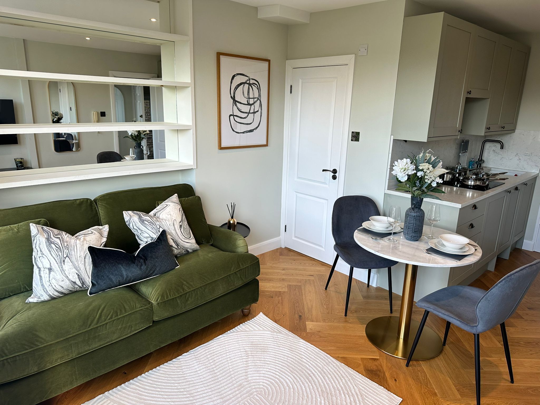 Una sala moderna con un sofá verde, una mesa de comedor redonda y una cocina con armarios y un lavamanos.