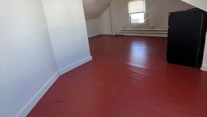 Une pièce mansardée spacieuse, avec un plancher rouge, des murs blancs et un plafond en pente.