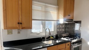Une cuisine avec des meubles en bois, un évier en acier inoxydable, un lave-vaisselle, une cuisinière et une fenêtre avec des stores.
