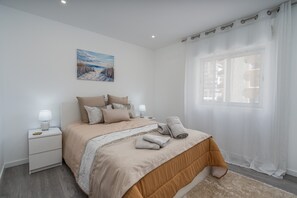 Un dormitorio con cama, mesitas de noche, lámpara, un cuadro y ventana con cortinas.