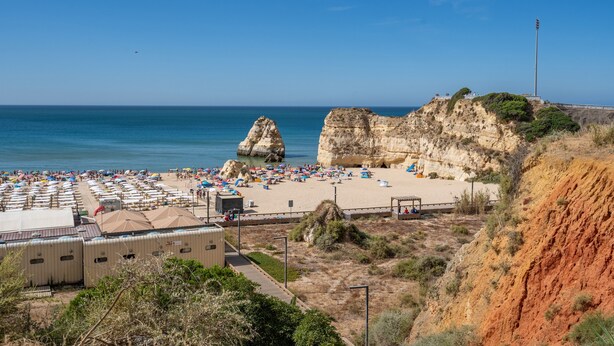 Una playa con un acantilado rocoso, una fila de sombrillas y algunas personas.
