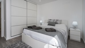 Un dormitorio moderno con un armario grande, una cama con cabecera gris y mesitas de noche con lámparas.