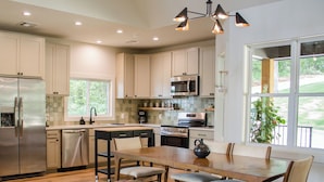A modern kitchen with a central island, stainless steel appliances, and large windows.