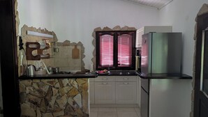 Eine Küche mit Steinwand, weißen Schränken, einem Edelstahlkühlschrank und einem Fenster mit Jalousien.