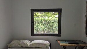 Ein Zimmer mit einem Bett, einem kleinen Tisch und einem Fenster mit Blick auf Grünflächen.