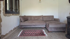 Ein Wohnzimmer mit einem braunen Ecksofa, einem gemusterten Teppich, einer Wand aus Naturstein und einer eingebauten Klimaanlage.