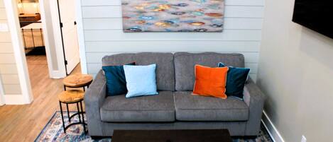 A living room with a grey sofa, two side tables, a coffee table, and a colorful rug.