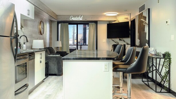 Una cocina moderna con una isla central, electrodomésticos de acero inoxidable y un comedor con taburetes de bar.
