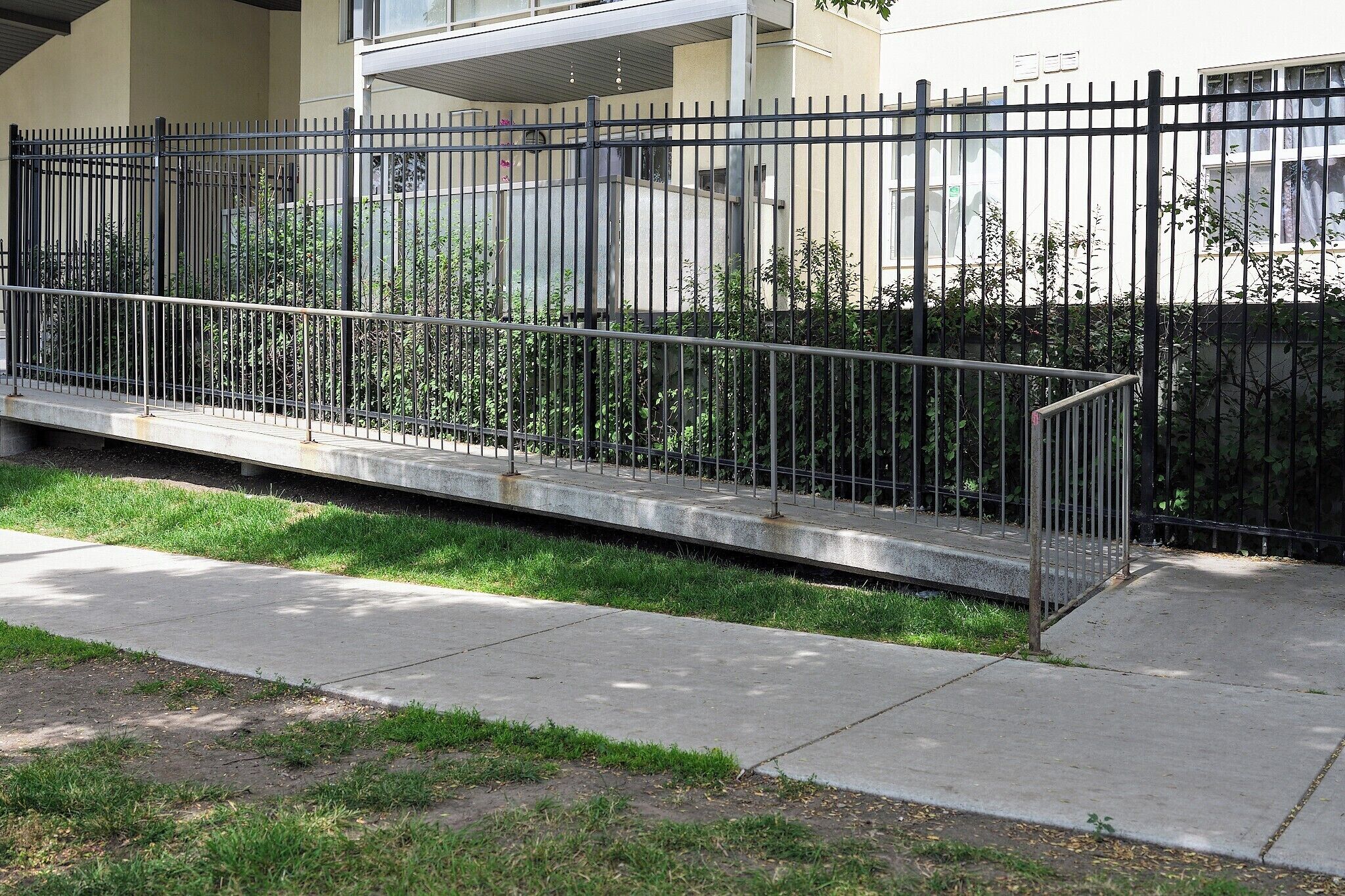 A black metal fence with vertical bars, a concrete pathway, and a grassy area.