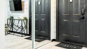 Una entrada moderna con una puerta de madera oscura, una puerta de cristal que da a una sala de estar, un televisor de pantalla plana montado en la pared y una pequeña mesa con plantas.