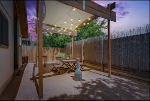 An outdoor patio area with a wooden pergola, string lights, a table, and benches.