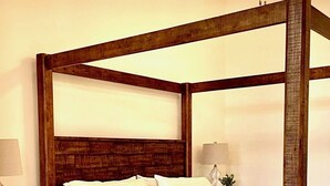 A four-poster bed with a wooden frame, white bedding, and a nightstand with a lamp and a vase with a plant. - Stunning new loft in historic Union Block. Brand new, walk to everything. (Brigham City)