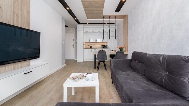 Ein modernes Wohnzimmer mit Flachbildfernseher, grauem Sofa und weißem Couchtisch mit floraler Unterlage.