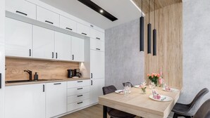 Eine moderne Küche mit weißen Schränken, einer Holzauskładung und einem Essbereich mit einem für zwei Personen gedecktem Holztisch.