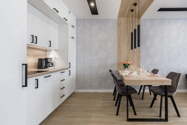 Una cocina moderna con armarios blancos, encimera de madera y un comedor con mesa de madera y sillas negras.