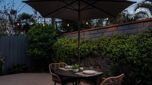 Une terrasse extérieure avec une table et des chaises, entourée de verdure et d’un mur en briques.