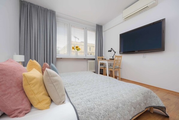 Un dormitorio con cama, escritorio, silla, televisor y ventana con cortinas.