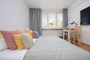 Un dormitorio con cama, escritorio, silla, ventana con cortinas y radiador.