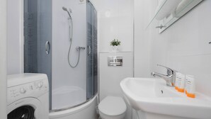 A modern bathroom with a glass-enclosed shower, a built-in washing machine, a toilet, and a sink with toiletries.