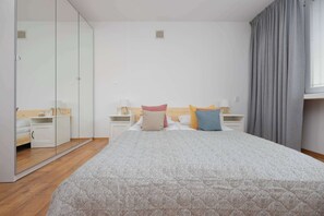 Un dormitorio con una cama grande, mesitas de noche, un armario y un espejo.