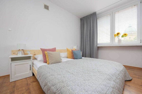 Un dormitorio ordenado con cama, mesita de noche y ventana con cortinas.