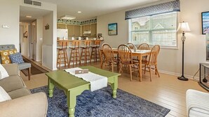 Een ruime woonkamer met een groene salontafel, een eethoek met houten stoelen, en een keuken op de achtergrond.