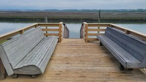 Een houten pier die uitkomt bij een rustig wateroppervlak, met bankjes aan beide kanten.
