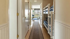 Een gang met witte deuren en een vloerkleed dat leidt naar een kamer met een bed en opbergplanken.