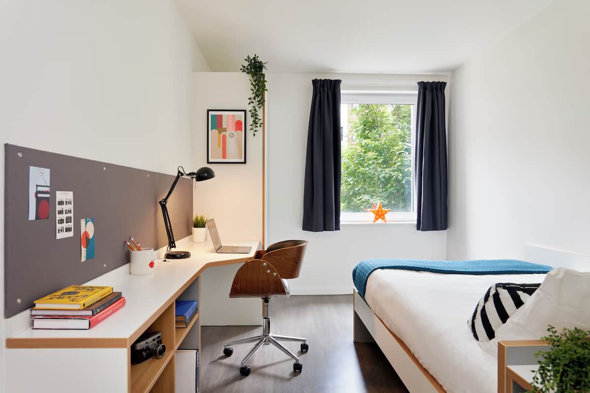 A modern bedroom with a desk, a laptop, a chair, a bed, and a window with curtains.