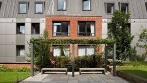 A modern building with a brick facade, multiple windows, and a green garden area with benches. - For Students Only - Modern Accommodation in Leeds City Centre (Leeds)
