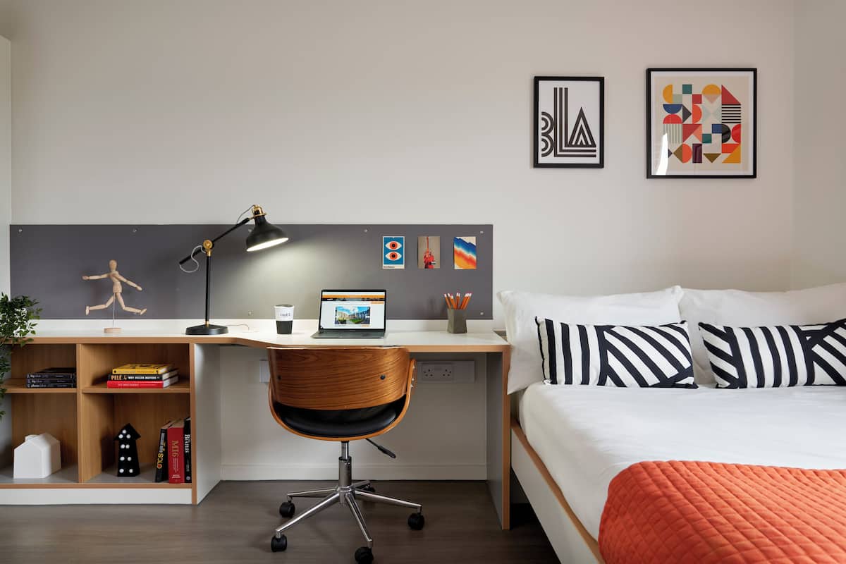 A modern bedroom with a wooden desk, a laptop, and a bed with striped pillows.