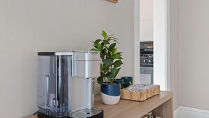 A kitchen area with a coffee maker, a potted plant, and a wooden shelf with items. - Cozy Dog-Friendly Boho Duplex (Lakewood)