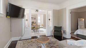 A modern living room with a flat-screen TV, a round wooden coffee table, a green armchair, and a bed with a white headboard. - Cozy Dog-Friendly Boho Duplex (Lakewood)