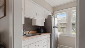 A kitchen with white cabinets, a stainless steel refrigerator, a black microwave, and a window with a view of a house. - Cozy Dog-Friendly Boho Duplex (Lakewood)