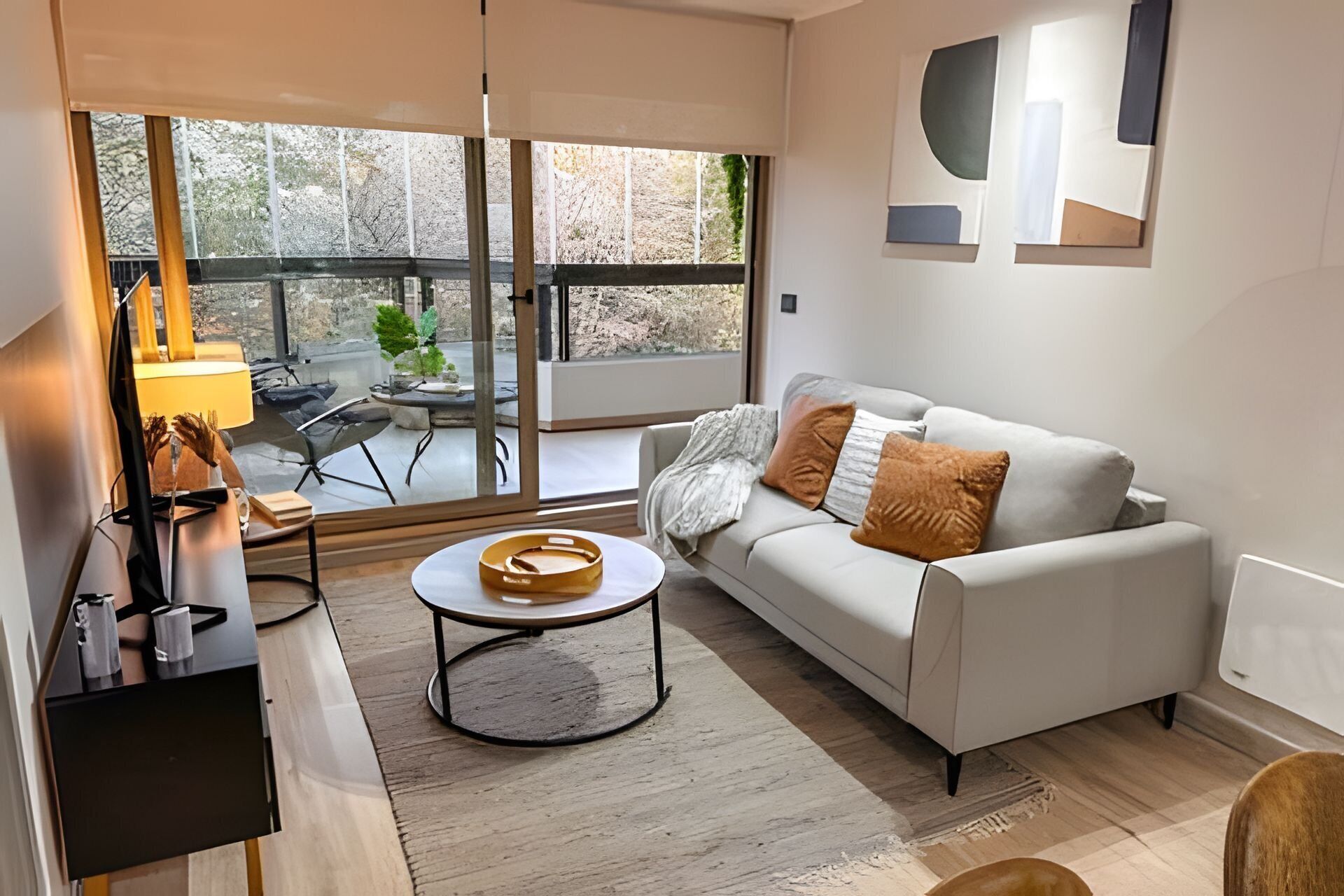 A modern living room with a white sofa, a round coffee table, and a glass door leading to an outdoor patio.