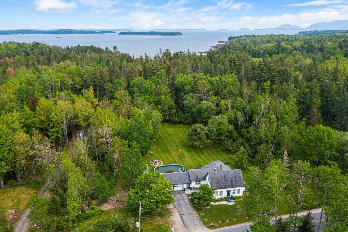 A house surrounded by dense forest with a view of a large body of water.