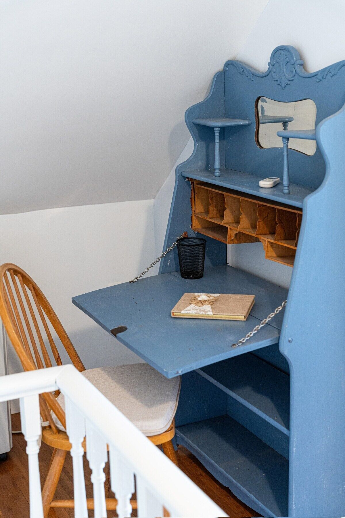 A blue desk with a chair, a small trash can, and a book on the desk.