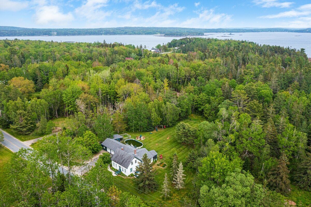 A house surrounded by dense forest, a clear view of the lake, and a well-maintained lawn.
