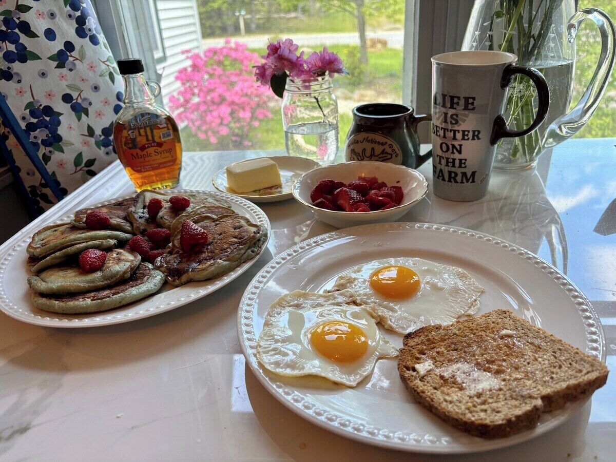 En frukostuppläggning med pannkakor, ägg, rostat bröd och en mugg på ett bord.