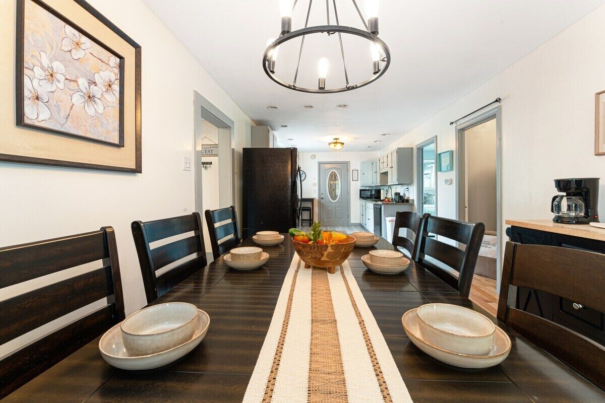 A dining area with a long table, chairs, a central fruit bowl, and a chandelier.