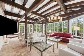 A spacious room with a high ceiling, large windows, and a mix of seating arrangements including a red sofa and white armchairs.